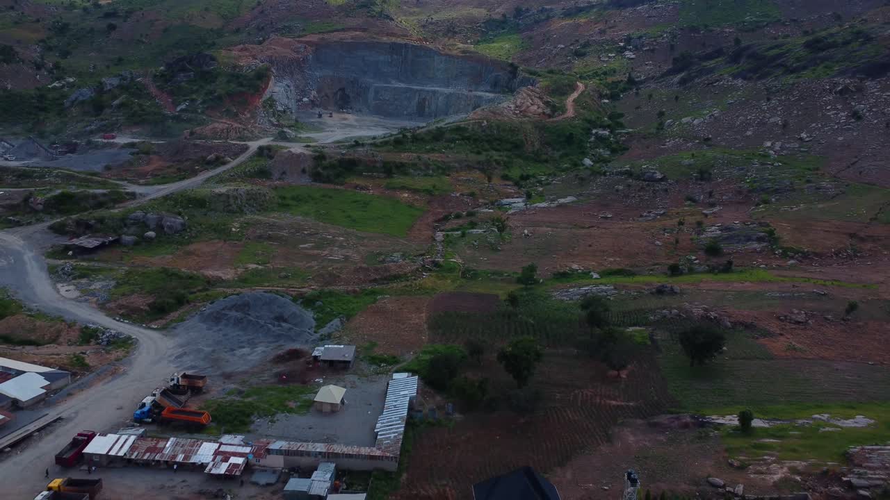 Drone reveals expansive quarry site in Abuja, Nigeria, displaying rugged terrain and machinery. Aerial highlights intricate layout of infrastructure under soft afternoon light in rural Africa