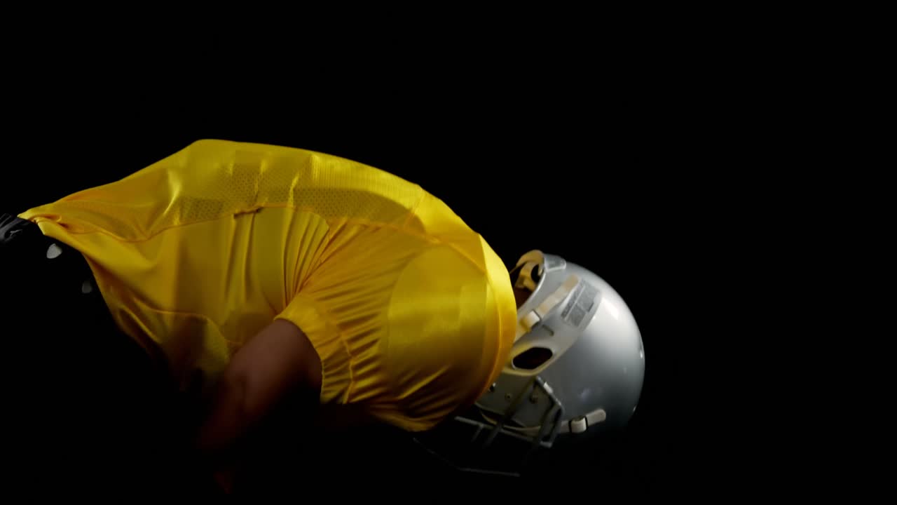 Giocatore di football americano piegato che tiene una palla sul campo con entrambe le mani 4K