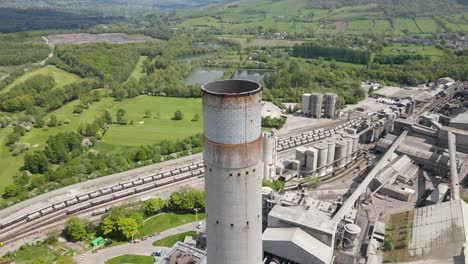 Vuelo-Aéreo-De-Drones-Alrededor-De-La-Chimenea-Principal-De-Las-Obras-De-Cemento-Breedon-Hope-Con-Una-Vista-Panorámica-Del-Distrito-Peak-Circundante