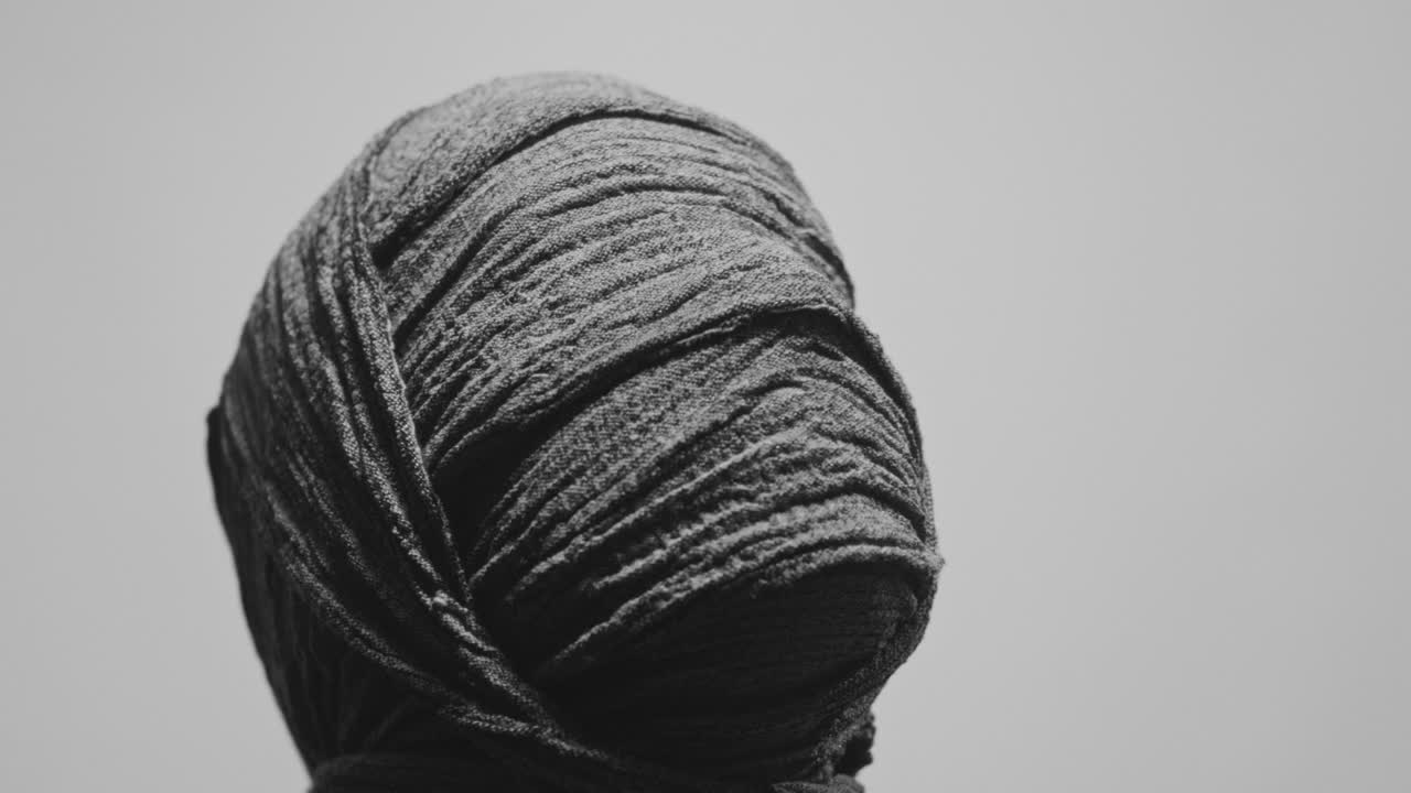 A mummy of a woman on a white backdrop looks up