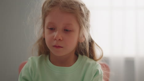 Calm-long-haired-child-taps-finger-playing-at-table-closeup