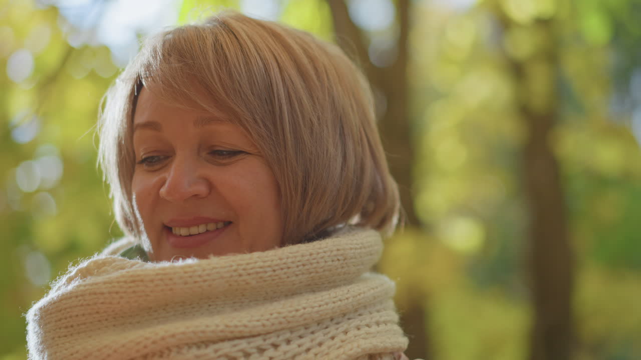 close up of woman admiring autumn leaf held up against sunlight creating glowing translucent effect highlighting warm seasonal colors and detailed veins in natural woodland setting