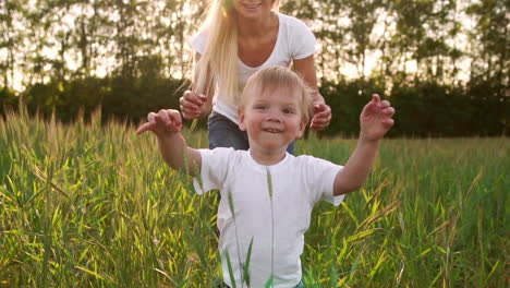 the concept of a happy family. in the rye field the kid walks across the field in the sun setting sun looking into the camera mom stands behind