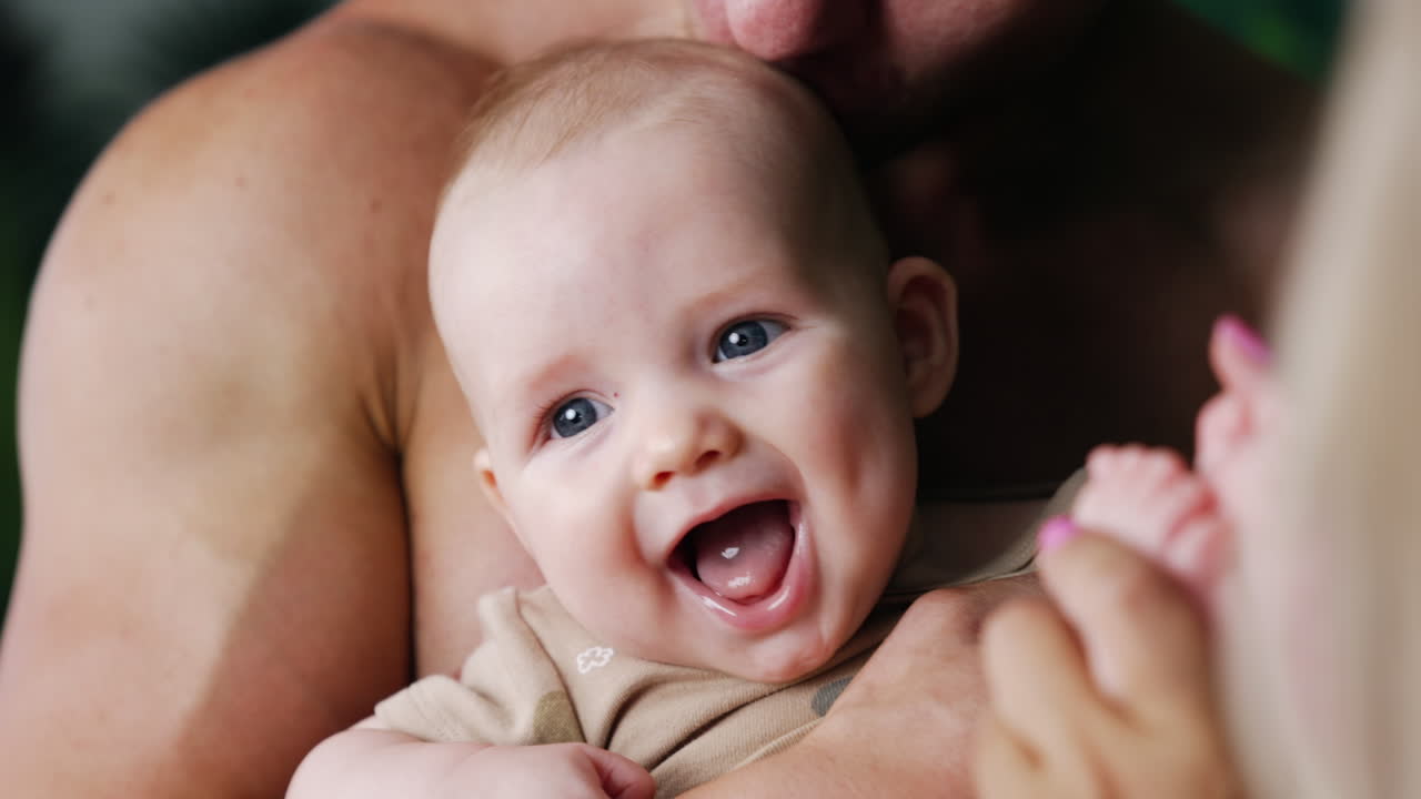 Adorable face of a Caucasian infant with grey eyes. Mom plays with son's hands and child is smiling sweetly. Close up.