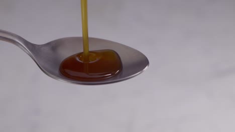 pouring throat, cough syrup medicine slowly in metal spoon