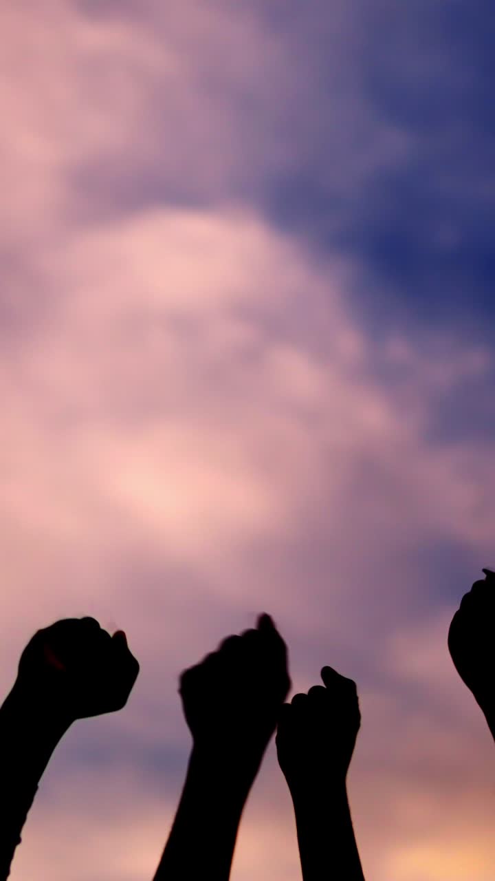 Fists of people raising angrily in the air facing sunset