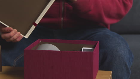 close up of man opening gift wrapped present in box from table in lounge at home