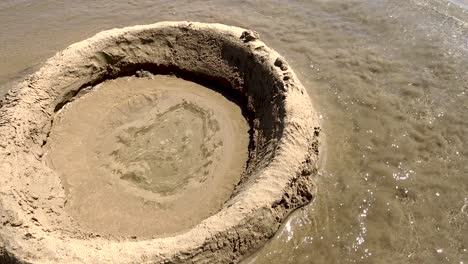 A-sand-wall-built-by-kids-stands-resilient-against-the-beach-waves-at-Costa-da-Caparica,-a-testament-to-family-summer-games-by-the-shore