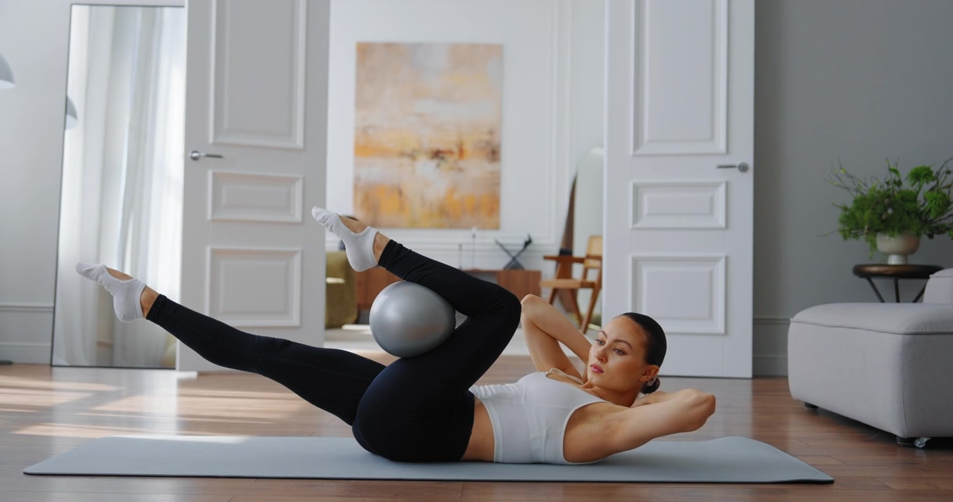 Giovane donna che esegue esercizi per il core con la palla da Pilates a casa