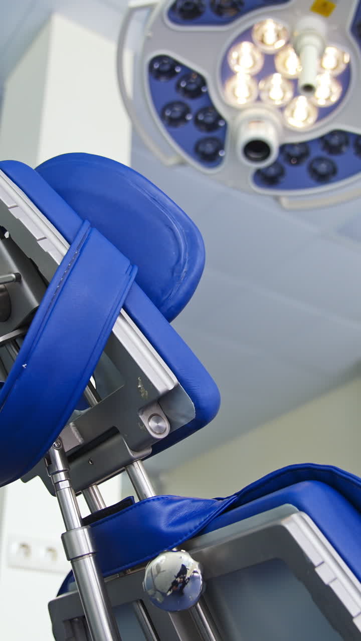 Folding chair with different appliances standing under the powerful lamp in dentist's cabinet. Close up. Low angle view. Blurred backdrop. Vertical video