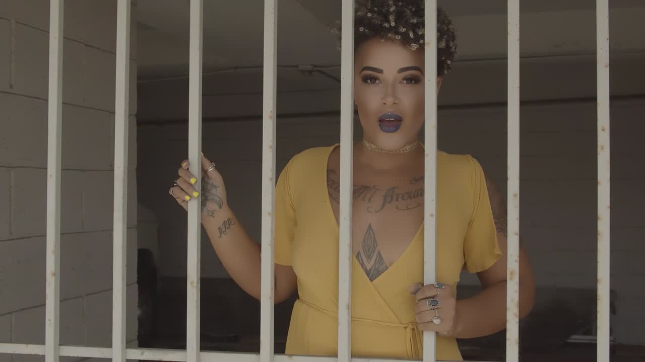 Latin woman with visible tattoos and sensual lips swaying behind prison bars. Zoom in