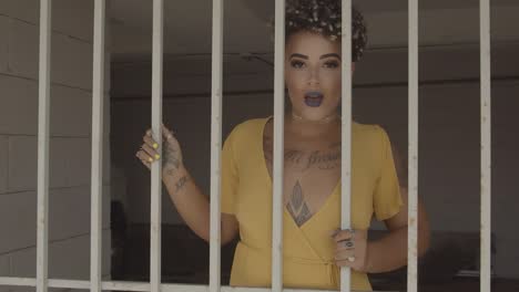 latin woman with visible tattoos and sensual lips swaying behind prison bars. zoom in