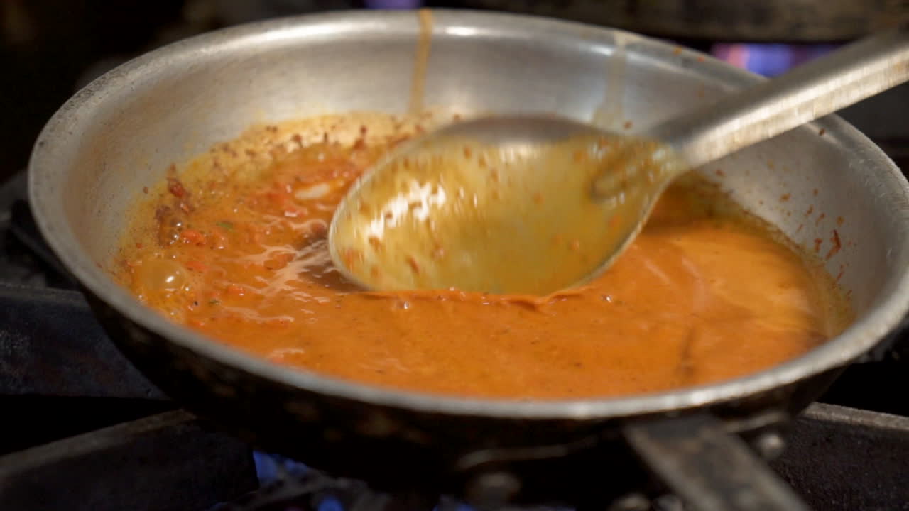 la cuchara remueve la salsa roja burbujeante en una sartén de acero inoxidable en la parte superior de la estufa, hd en cámara lenta