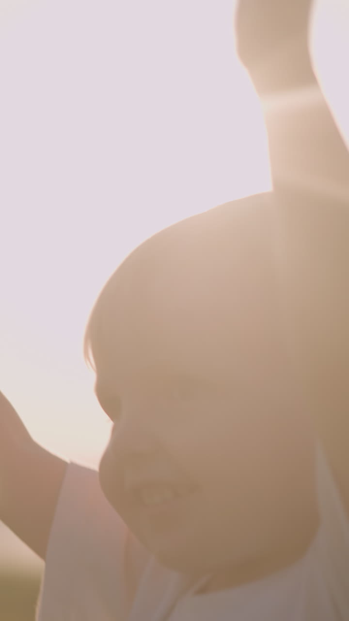 A joyful little boy in a white shirt walks through a sunny grass field with his hands raised, his face beaming with happiness, capturing a pure moment of childhood joy and wonder in nature