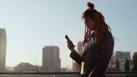 focused woman looking at phone screen. stylish girl holding cellphone outdoor.
