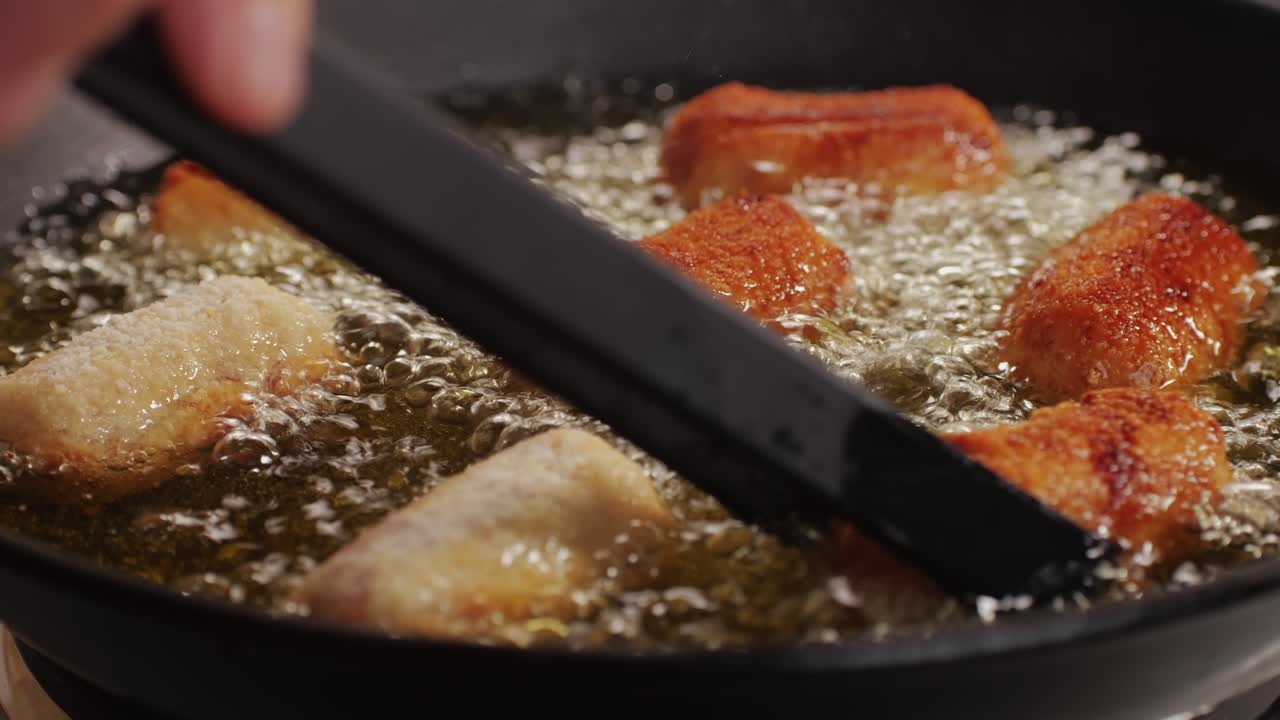 Portuguese croquettes broiling on black frying pan close-up macro. Breaded croquette of fish, potatoes and ham. Man cooking spanish food. High quality 4k footage