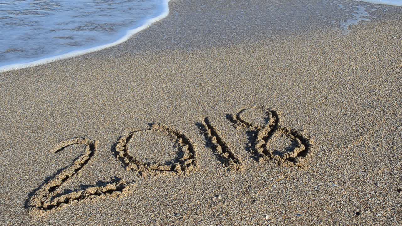 Inscripción 2018 en la arena. La inscripción es borrada por una ola del mar. Grabación en la playa.