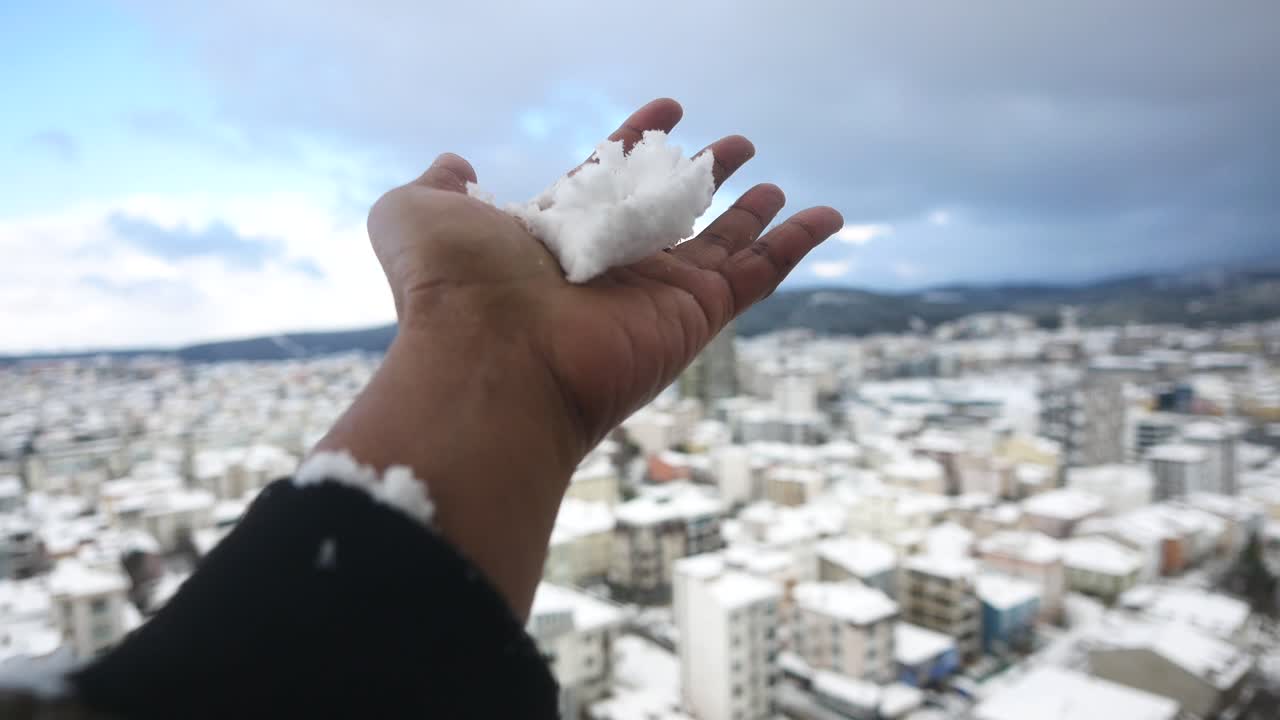 Hand holding snow in a city covered in snow