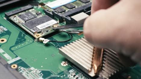 technician using tweezers unscrew and unplug cables from wireless card from laptop motherboard