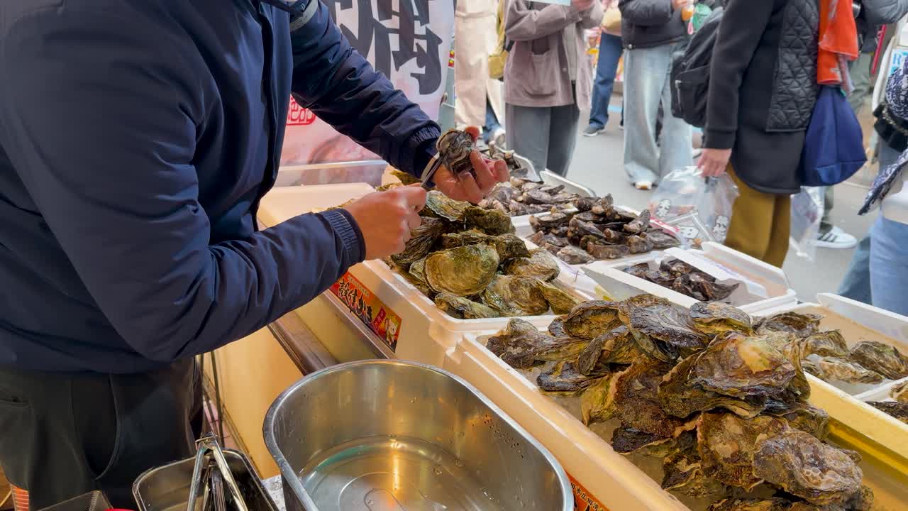 A vendor shucks fresh oysters at an outdoor market stall in Tokyo, Japan
