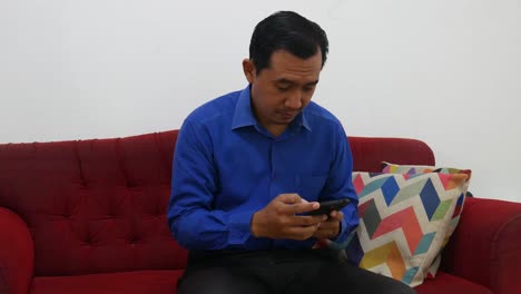 An-asian-businessman-receives-good-news-from-his-cell-phone-while-sitting-on-the-red-sofa