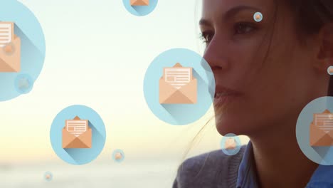 Animation-of-message-icons-floating-over-close-up-of-a-caucasian-woman-blowing-sand-at-the-beach