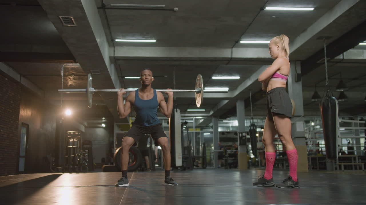 vista distante de una mujer caucásica monitor y un atlético afroamericano en el gimnasio.