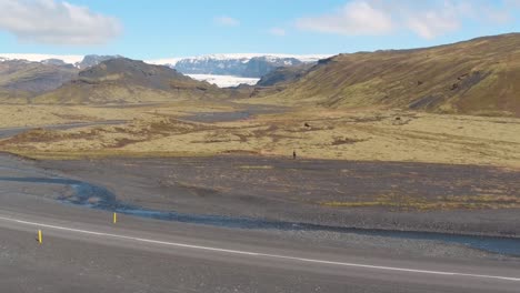 person walking, myrdalsjokull glacier in background. aerial flying backwards