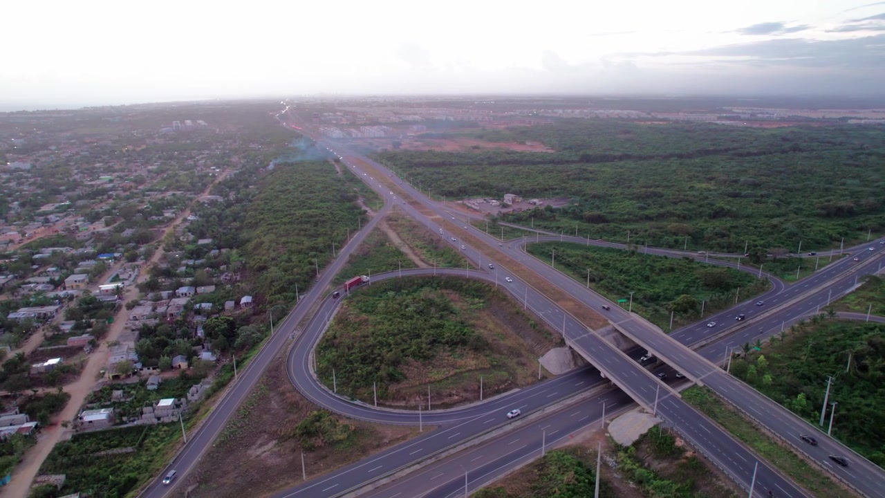 Ripresa aerea con drone dall'alto che avanza su uno svincolo autostradale al tramonto, catturando un semirimorchio che percorre una rampa a anello e veicoli che attraversano cavalcavia
