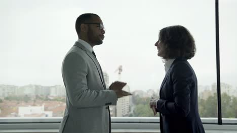 smiling colleagues standing near window and talking.