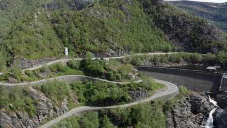 aerial flying backwards reveal small dam and winding roads on the hill - bergsdalen