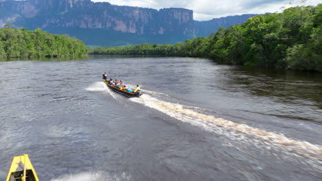longboats carrying tourists on a river in the amazon rainforest with towering tepuis in the background