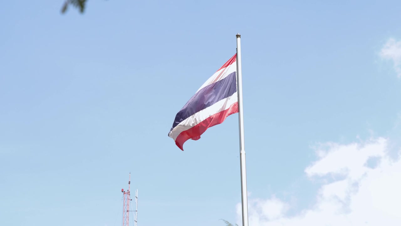 La bandiera nazionale thailandese sventola costantemente su un'asta d'argento sotto una luce solare intensa e nuvole.
