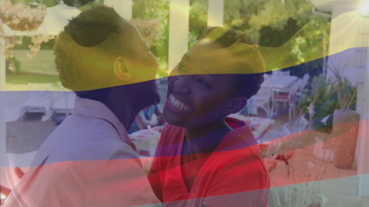 Animation of flag of colombia over happy african american family embracing in garden