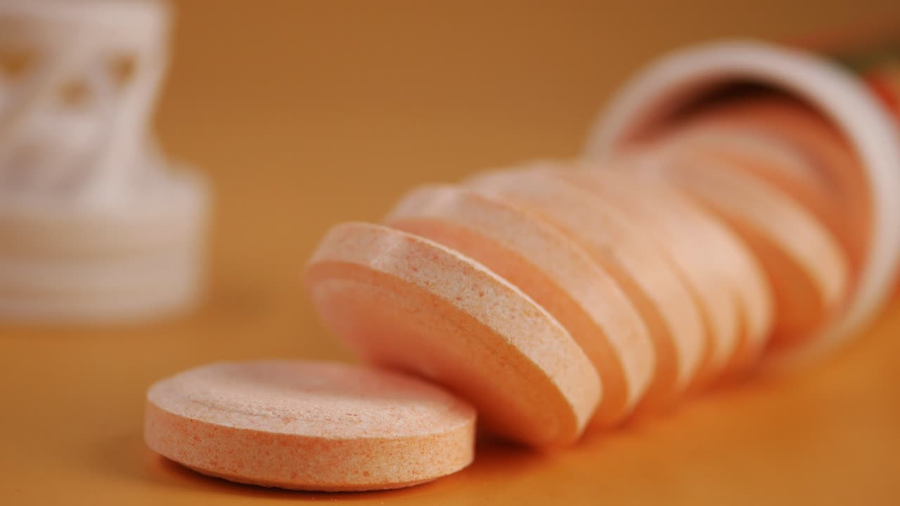 Compresse effervescenti di vitamina C arancioni che fuoriescono da un flacone