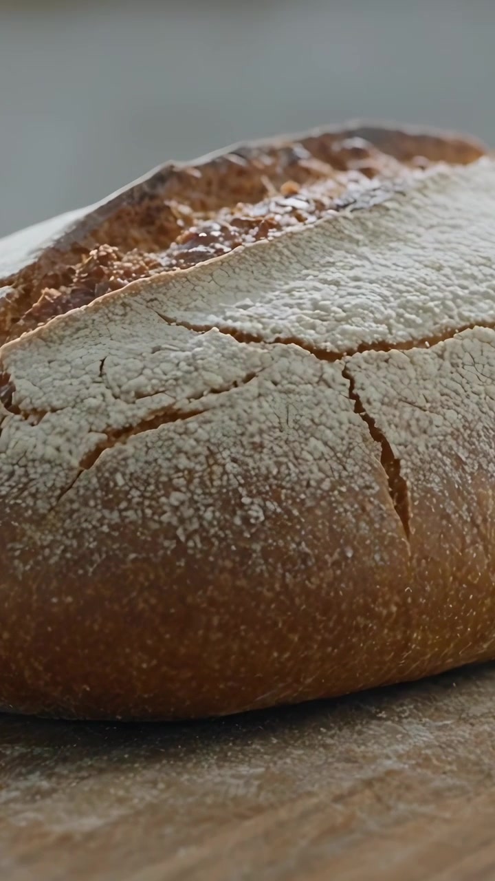 Vertical video: Zooming camera moving closer to rustic loaf on wooden board, showing cracked crust