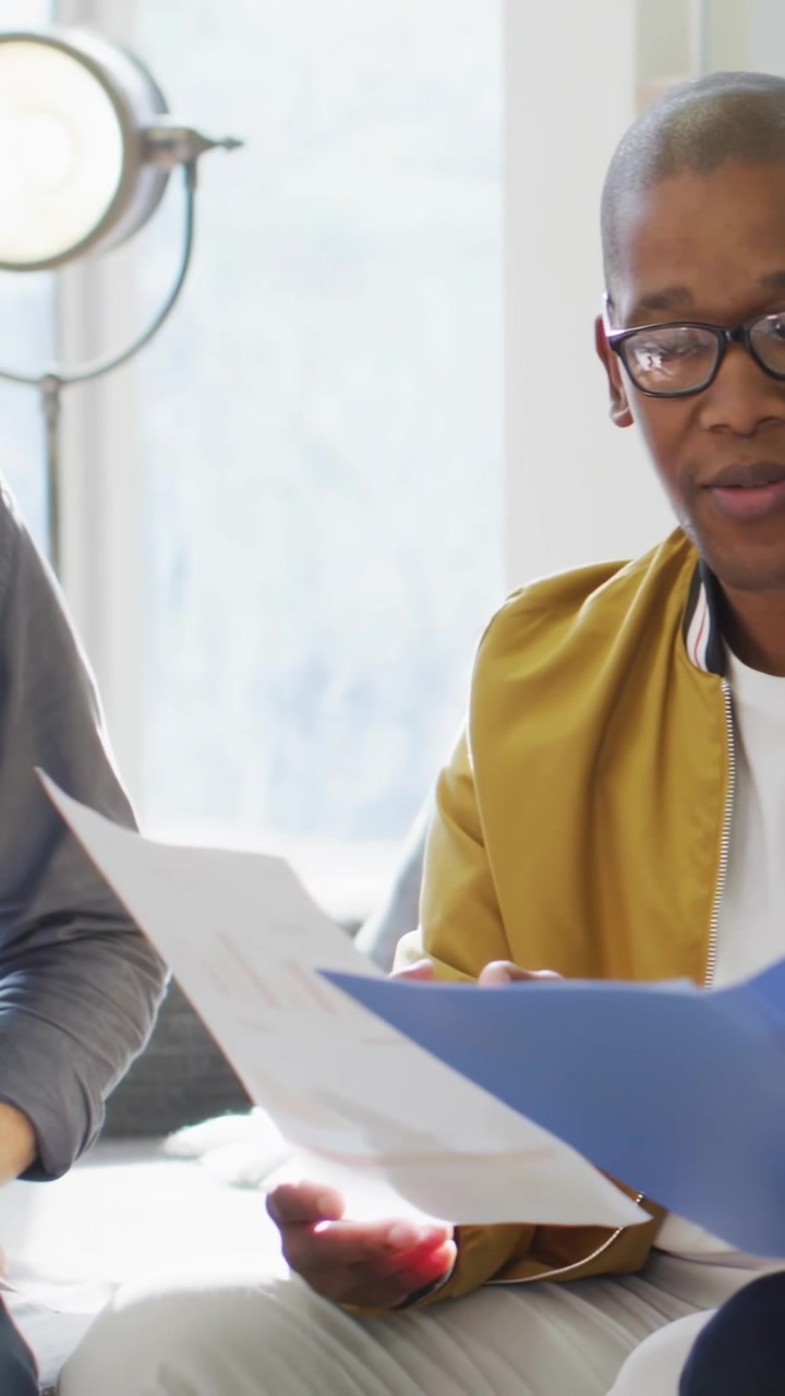 Vertical video: Seated man and peer sharing papers as social badges popping urging marketing review