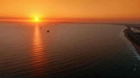 shore of the pacific ocean at sunset. los angeles beach from aerial perspective. orange sky above the horizon over the vast waterscape.