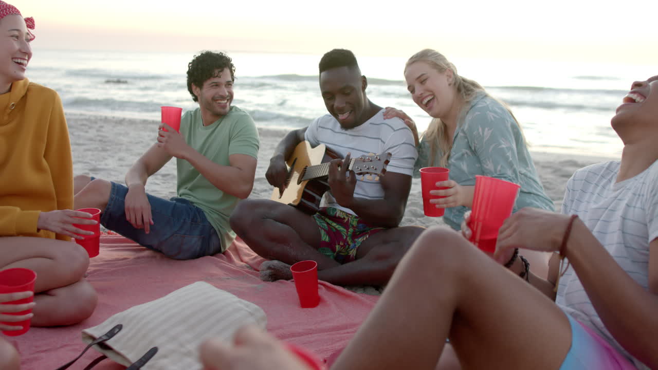 Amici di diverse etnie si godono un raduno in spiaggia al tramonto.