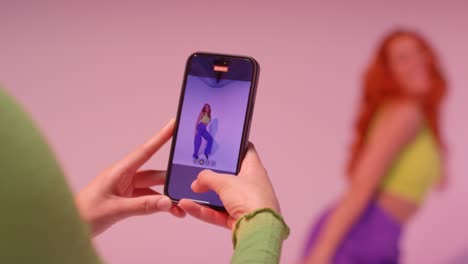 studio shot of woman taking photo of friend dancing on mobile phone against pink background 5