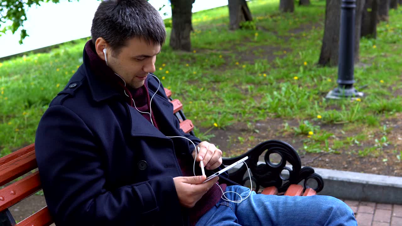 A man listens to music and works on a tablet in the park.