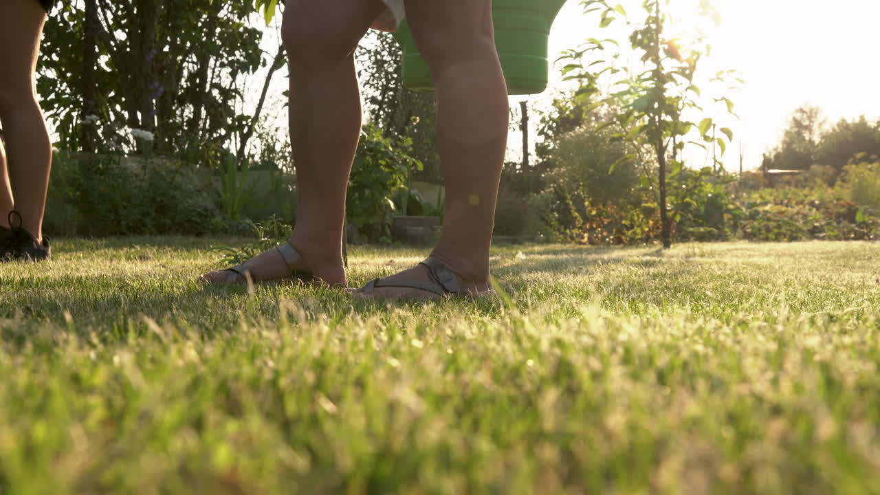 양동이를 들고 정원의 초원에 서 있는 검은 운동화와 침목을 입은 소녀와 여성