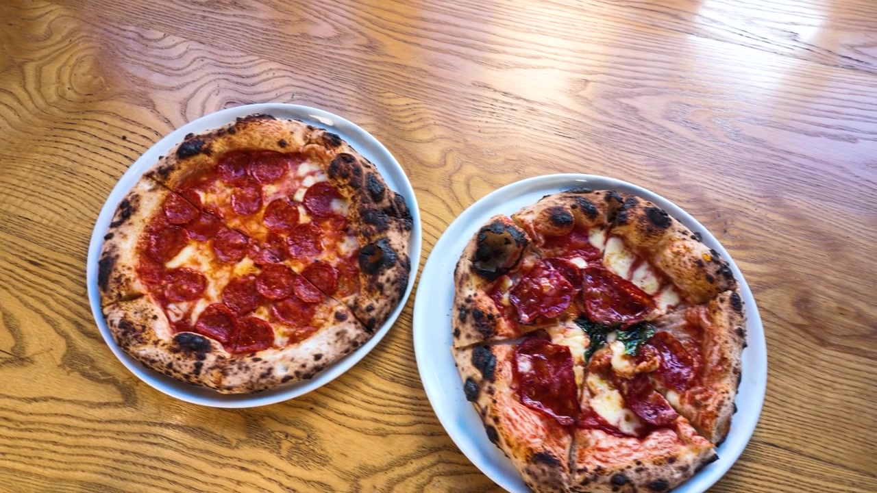Ripresa dall'alto di pizze al salame piccante e al prosciutto su un tavolo di legno con illuminazione naturale.