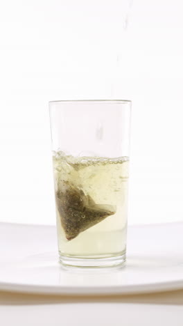 verter agua caliente en un vaso con una bolsa de té, en un plato blanco, fondo blanco