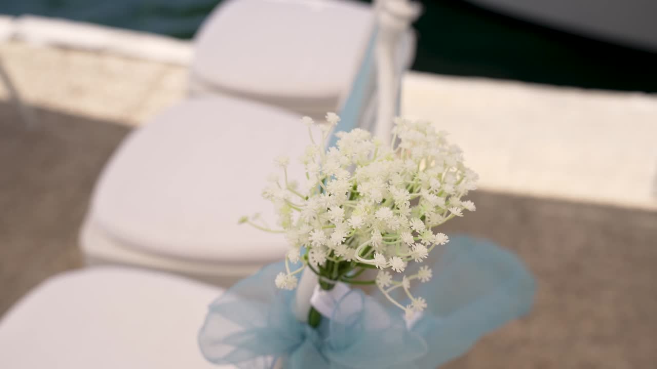 Delicati fiori bianchi adornano le sedie di un'affascinante location per matrimoni all'aperto vicino all'acqua. Dettagli in azzurro creano un'atmosfera romantica, perfetta per la cerimonia.