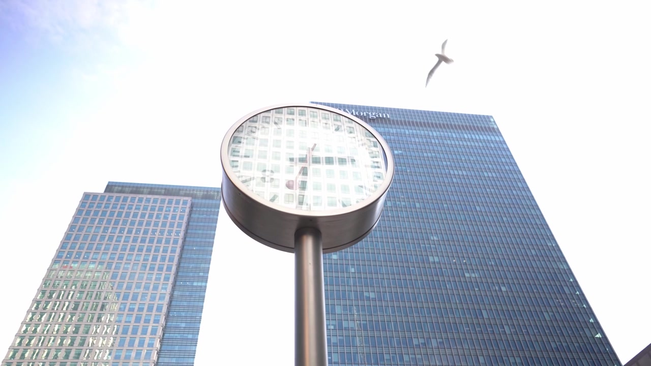 Inquadratura dal basso di un orologio su palo a Canary Wharf con grattacieli sullo sfondo.