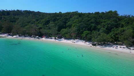 tourists enjoying the white sand kaoh touch beach and turquoise waters of koh rong, a tropical island paradise in cambodia. spectacular aerial view flight wide orbit overview drone