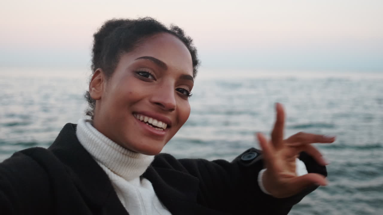 una chica afroamericana feliz haciendo una llamada de video junto al mar.