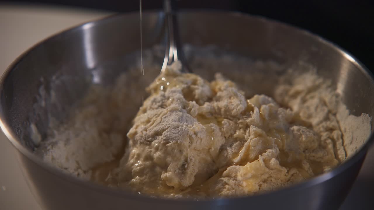 Pouring Oil into Dough in a Metal Bowl