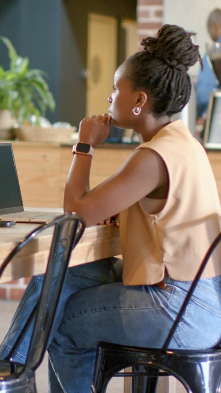 Vertical video: Explaining woman in tan vest gesturing to passing staff behind cafe bar with laptop
